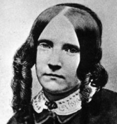 A photo of SFC as a young girl. She looks quite serious for her age - maybe 10. She has dark wide-set eyes, and her mouth is in a straight line. Her hair is parted in the middle. The sides hang in long curls and cover her ears. The back is in a bun.