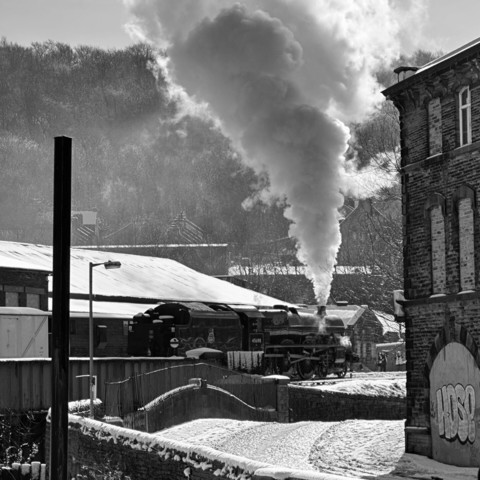 Square photos showing steam train number 45690, Leander backs onto its train at Keighley station on the Keighley & Worth Valley Railway. There is snow on the ground and a plume of steam coming from the chimney.