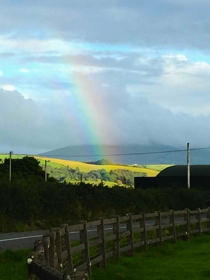 Rainbow over green rolling farmland. Wood fence enclosing pasture in foreground.
