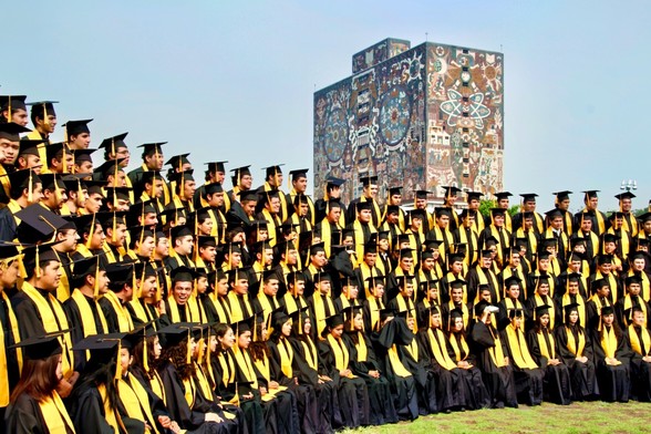 Daytime image of a crowd of recently graduated engineers, all dressed up in black and yellow; in the background the imposing building of the UNAM, University of Mexico, library all covered in mosaics representing Mexican cosmogony.