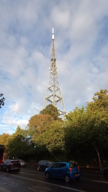 The Crystal Palace Transmitter Tower stands proud in the evening sunshine beneath a smear of emptied clouds.
In the foreground lies Crystal Palace Parade, a tree-lined avenue of potential loveliness, slick with oily water and a garish selection of steel-and-plastic mobility aids.