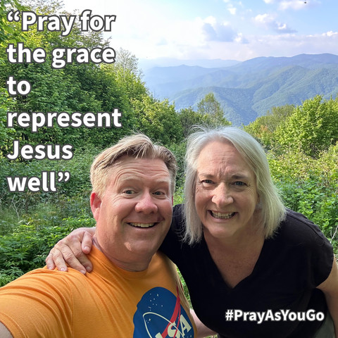 A smiling man and woman pose for a selfie outdoors, surrounded by green foliage and mountains in the background. The image features the quote, "Pray for the grace to represent Jesus well," and includes the hashtag #PrayAsYouGo.