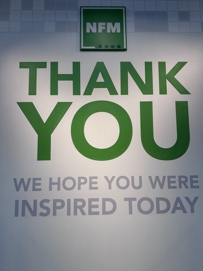 A wall display featuring the text "THANK YOU" in large green letters, accompanied by smaller gray text that reads "WE HOPE YOU WERE INSPIRED TODAY." The logo "NFM" is displayed above the text.