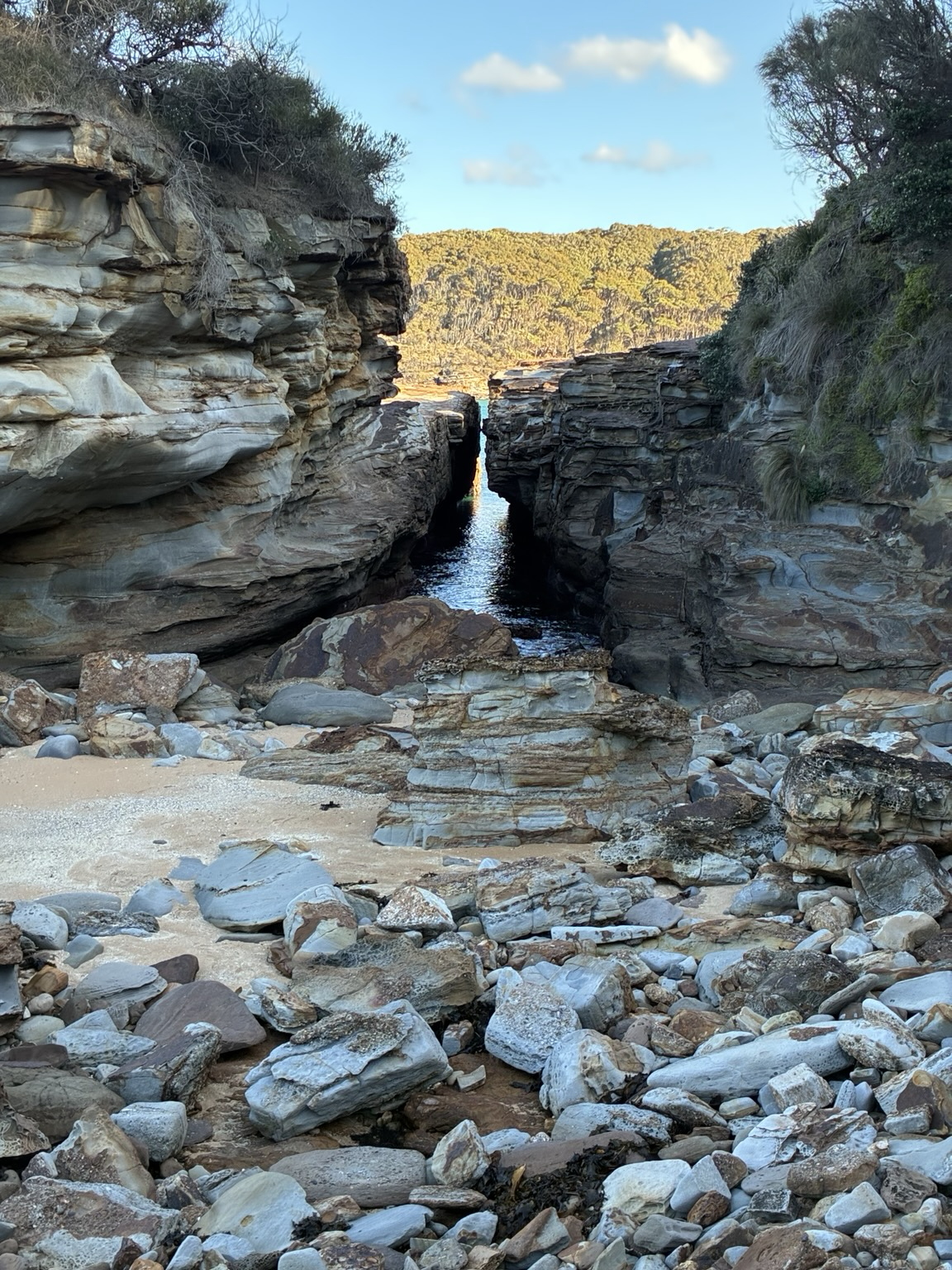 Rocks in the four ground with a view through a crack to the bay and bush beyond