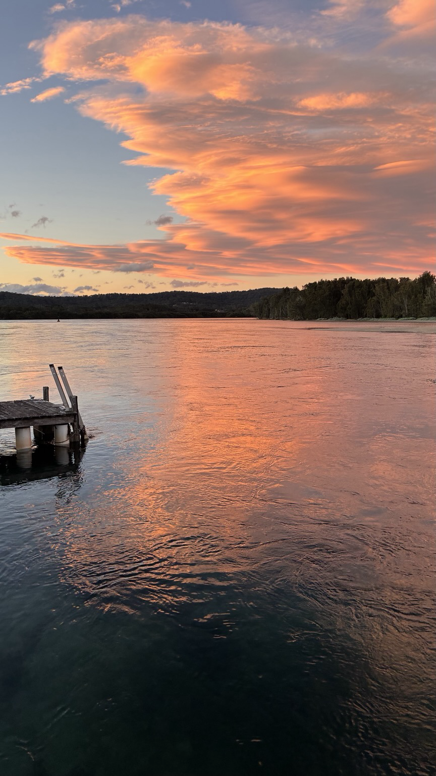 Beautiful orange sunset clouds reflected in the water of a river with a jetty on the left